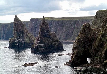 Cliffs along a rugged coastline with large sea stacks rising from the ocean.