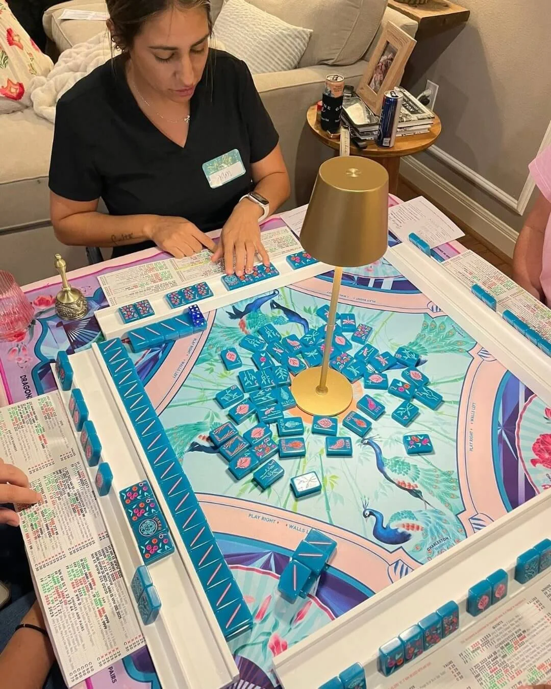 People playing mahjong around a table with a colorful tropical-themed game board and blue tiles.