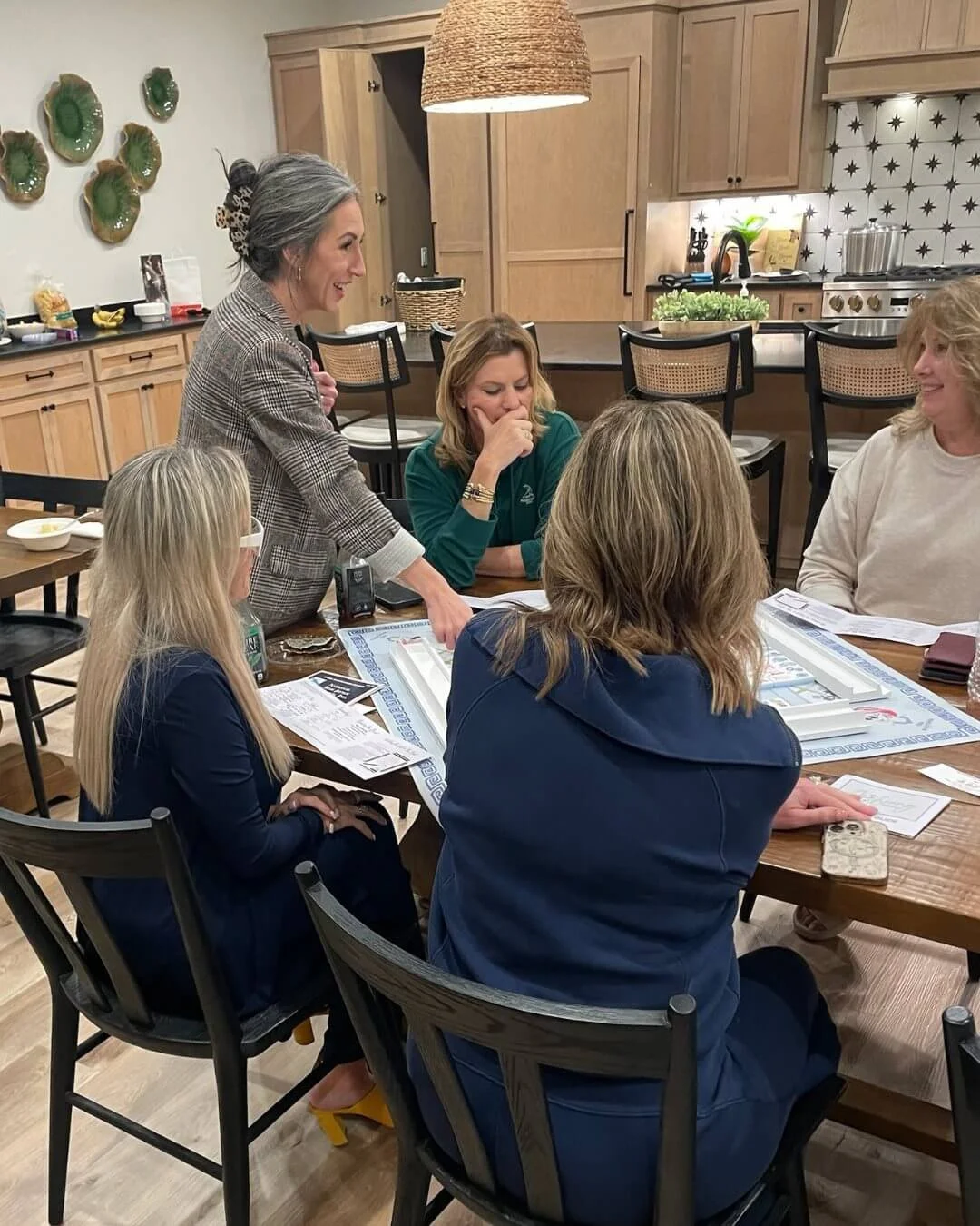 A group of women gathered around a dining table playing a board game in a cozy kitchen and dining area.