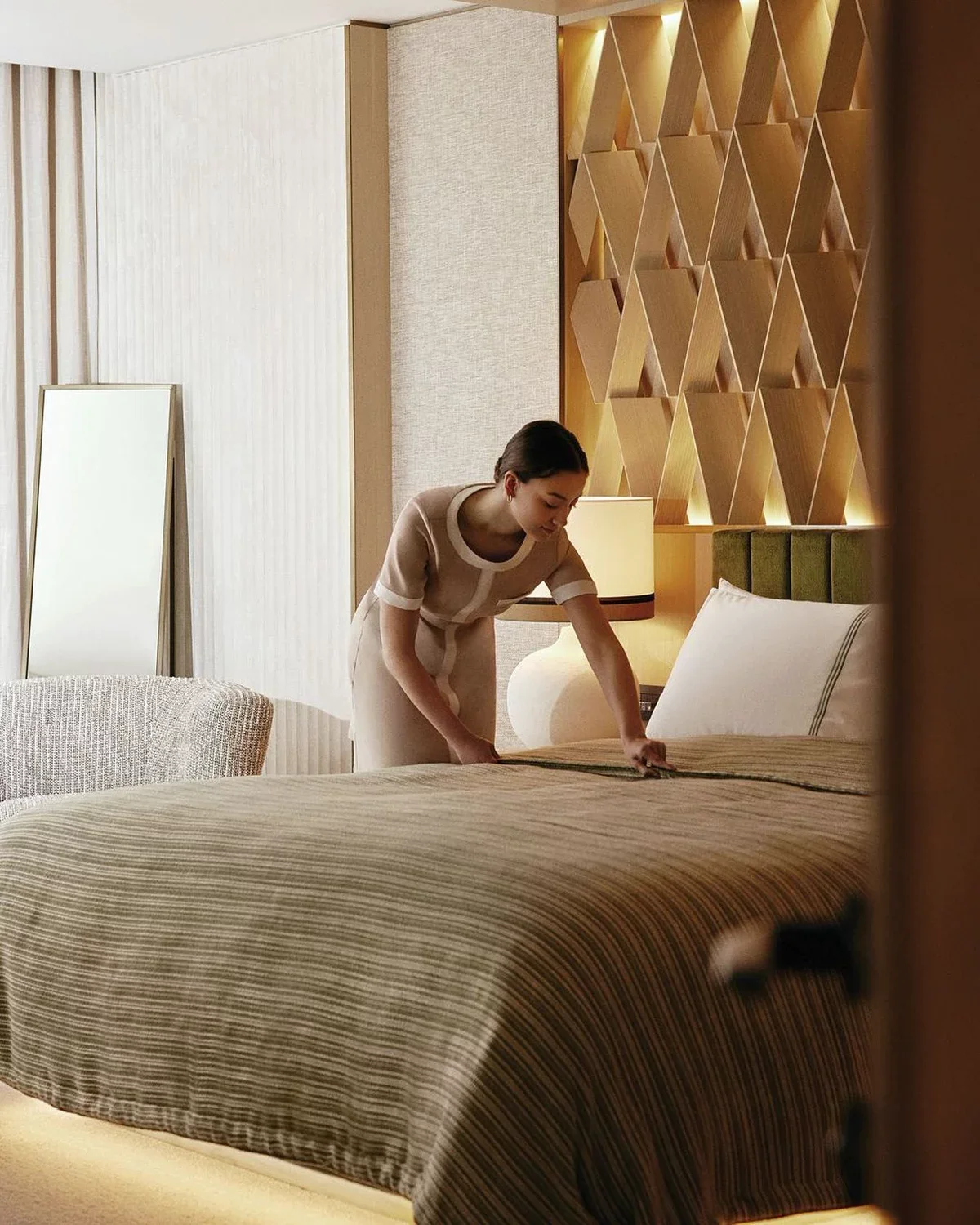 Mulher arrumando a cama em um quarto de hotel.