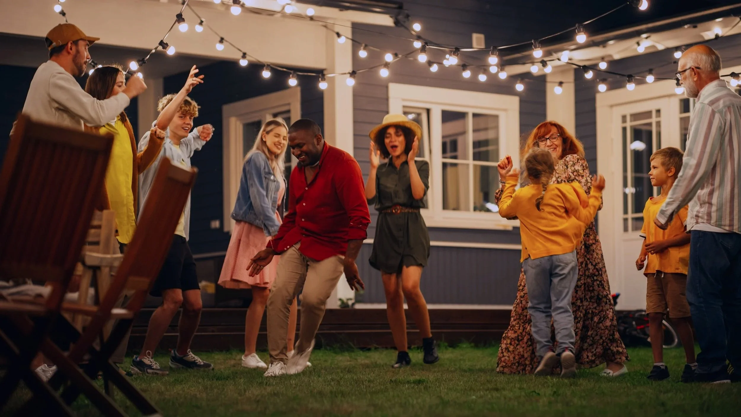 People dancing and celebrating outdoors under string lights at night, in front of a house.