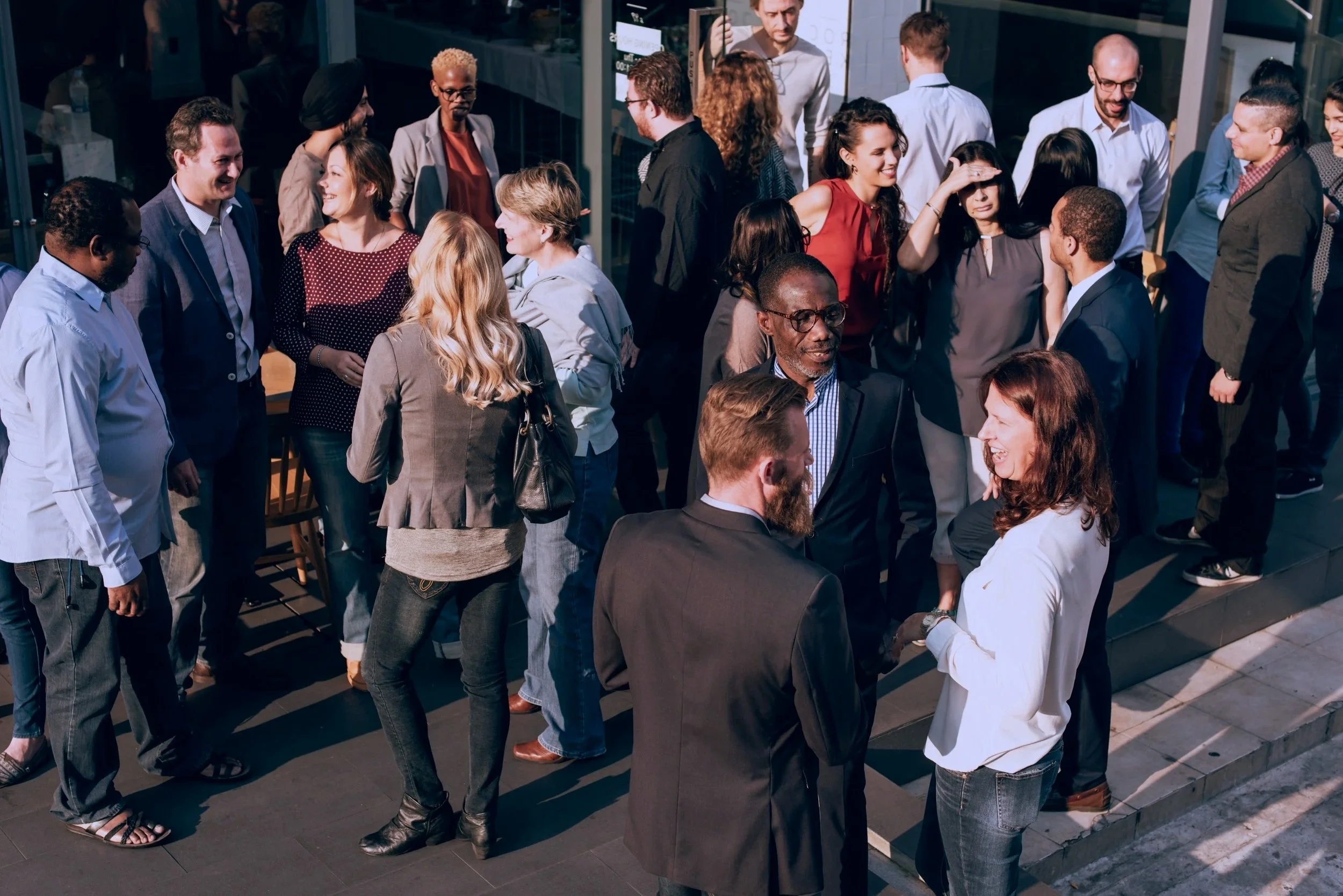 Group of company employees socializing outside a building, some talking in small groups and others in pairs, during a professional networking event.