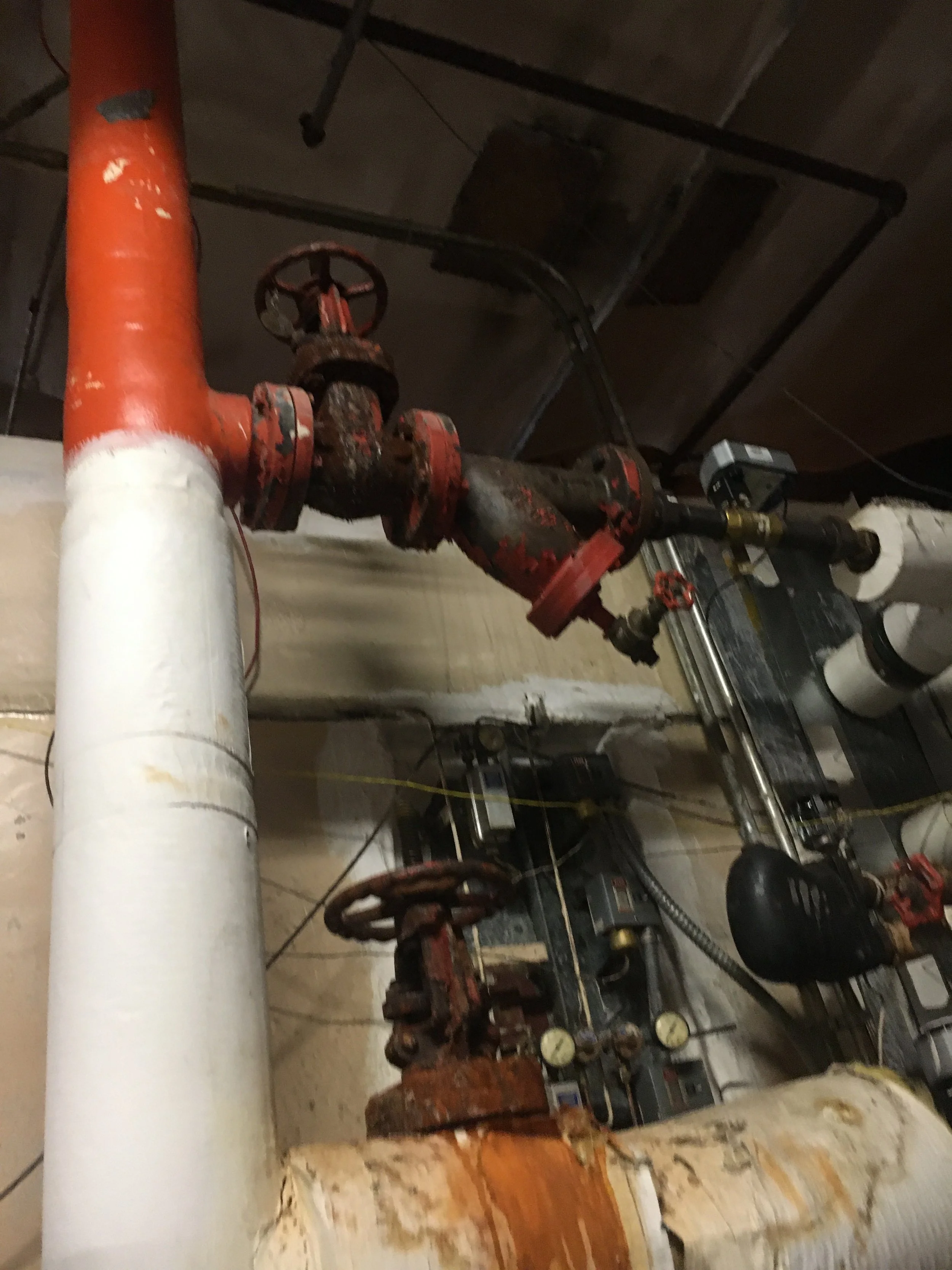 A network of elevated red and white pipes with valves, gauges, and a motor, installed along a ceiling in an industrial or mechanical room.