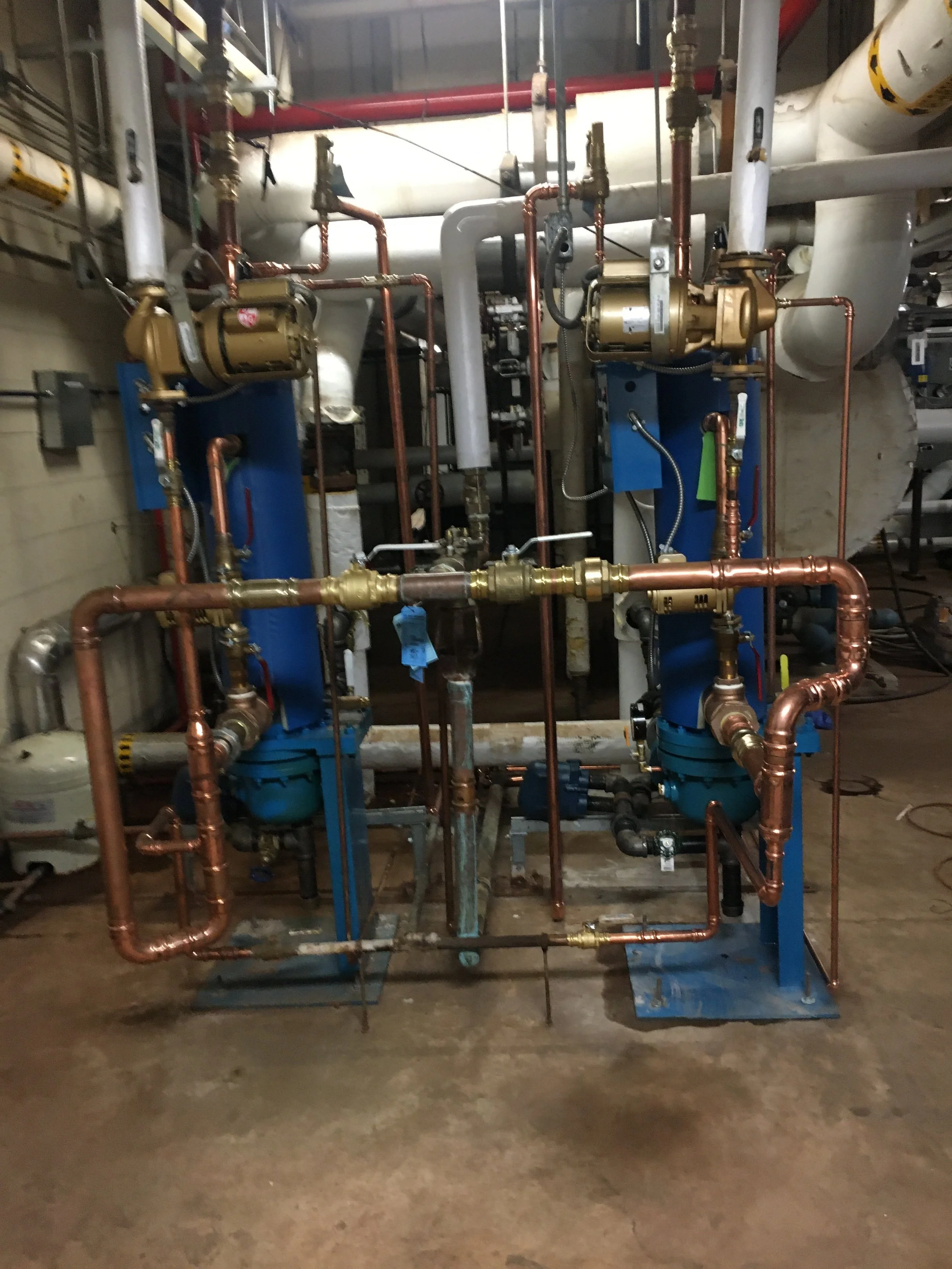 Industrial chiller or pump system with copper pipes, valves, and blue components in a mechanical room.