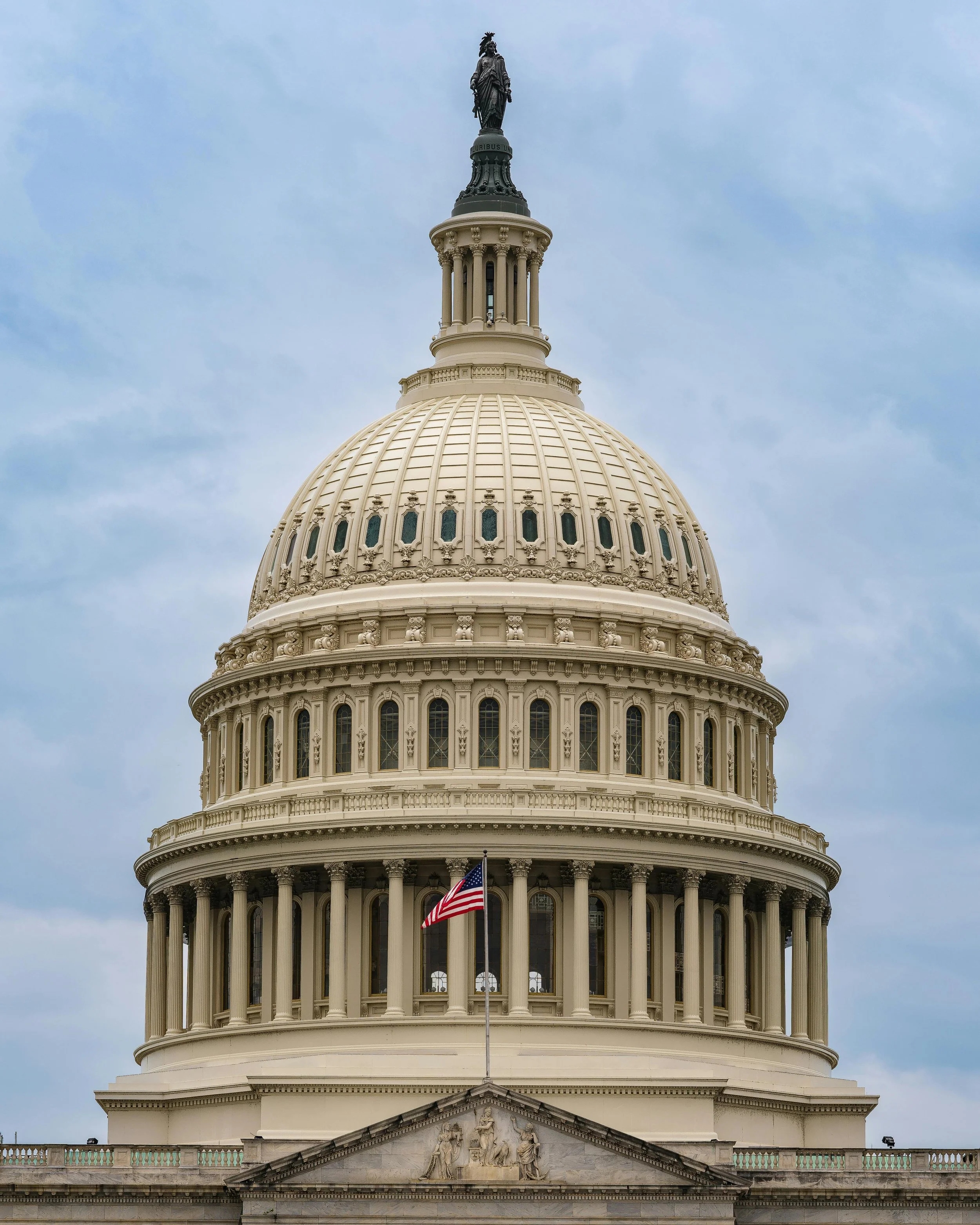 Front view of the United States Capitol building with a flag flying in front.