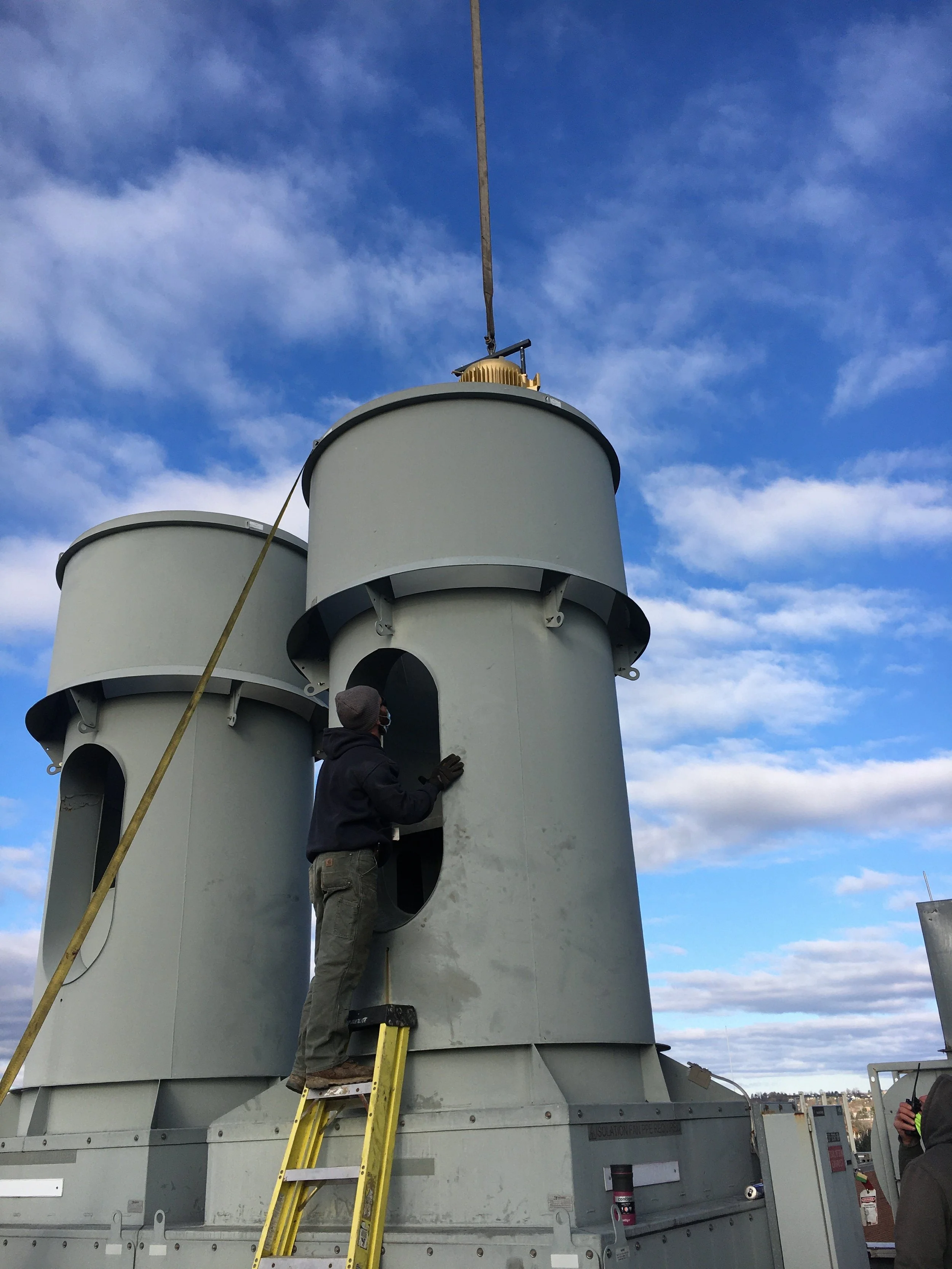 Person working on large industrial equipment outdoors against a partly cloudy sky.