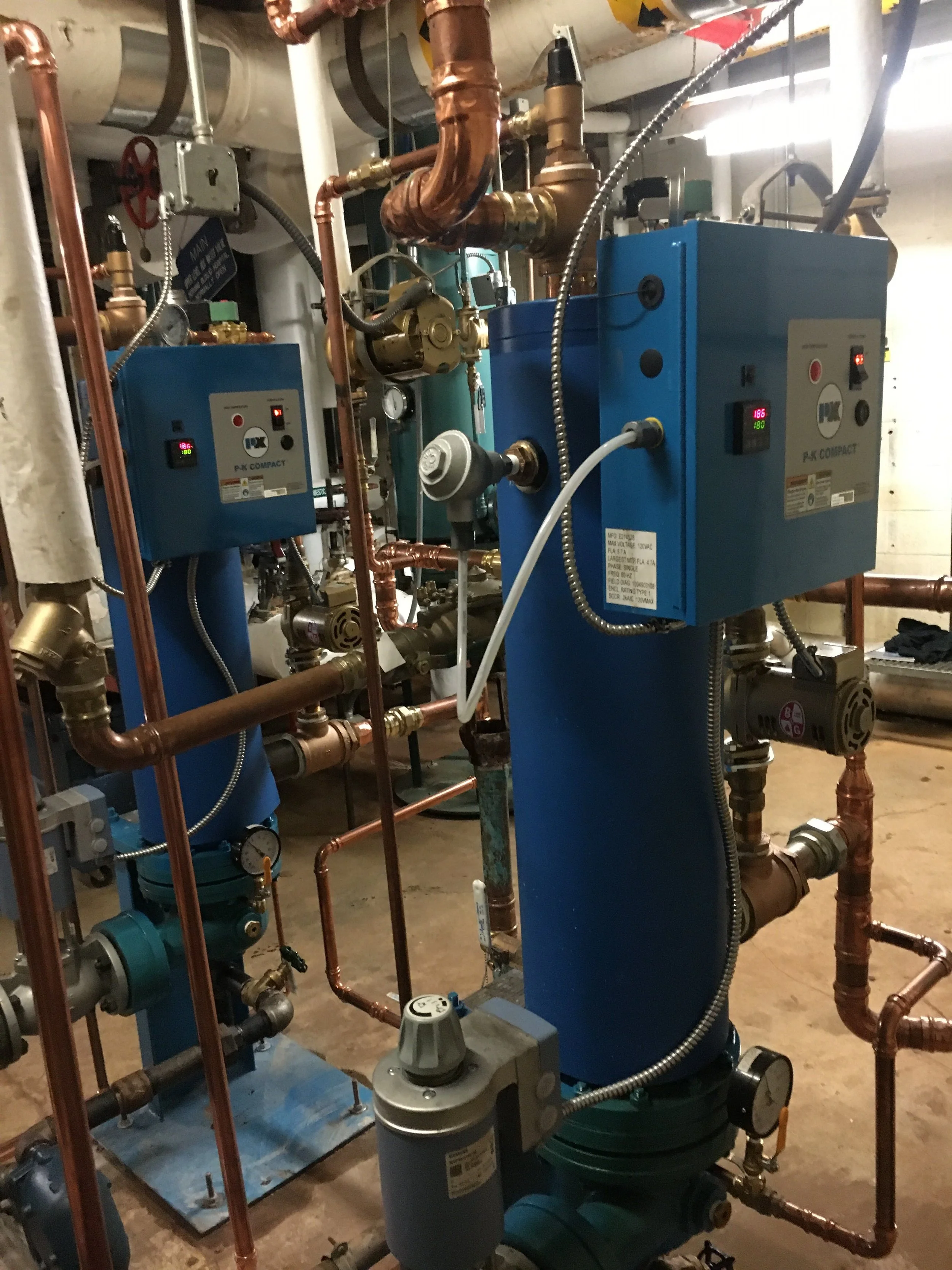 Industrial mechanical equipment with pipes, gauges, and control boxes in a utility room