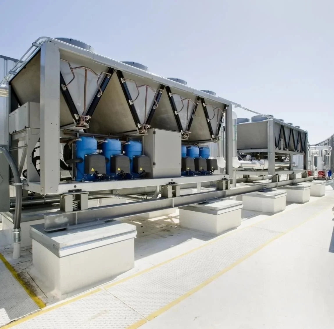 Industrial HVAC equipment on a rooftop with blue compressors and metal vents under a clear sky.
