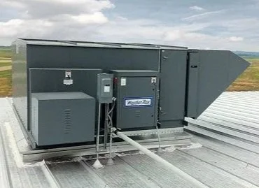 An industrial HVAC unit installed on a building roof, with duct connections and electrical components visible.