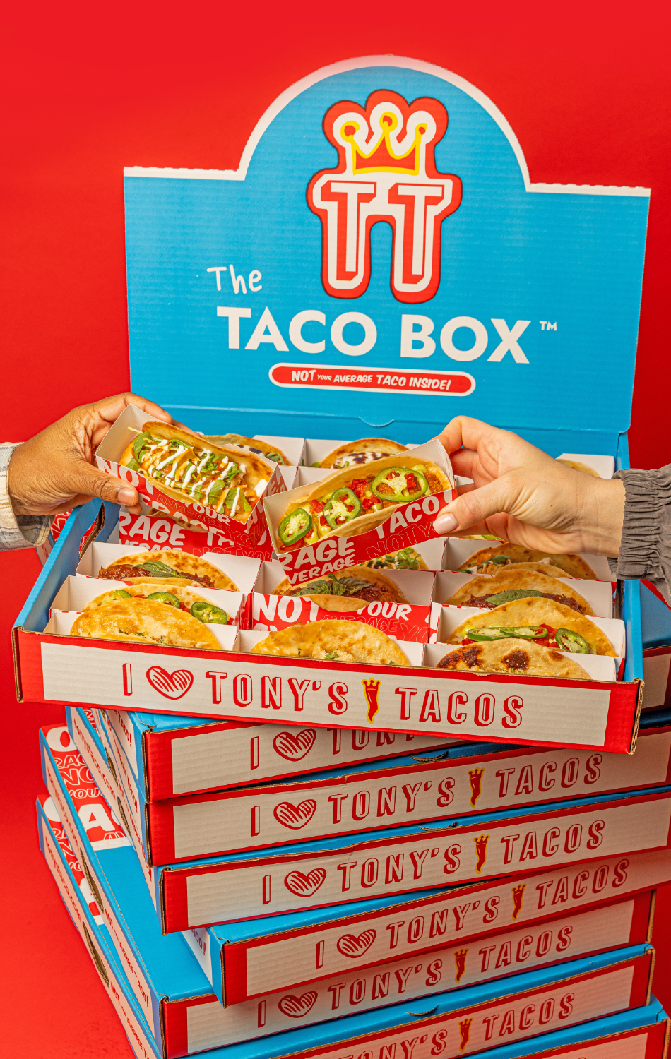 Close-up of a cardboard box labeled 'The Taco Box' filled with various tacos, with hands reaching in to pick some tacos, against a red background.