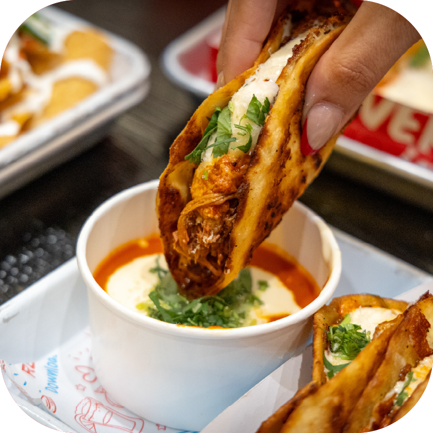 Close-up of a hand holding a SCARPETTA - 3 delicious garlic and oil mozzarella tortillas with braised beef, cheese, and pomodoro sauce, a touch of cilantro, served with Tony's Tacos secret Scarpetta dipping sauce.