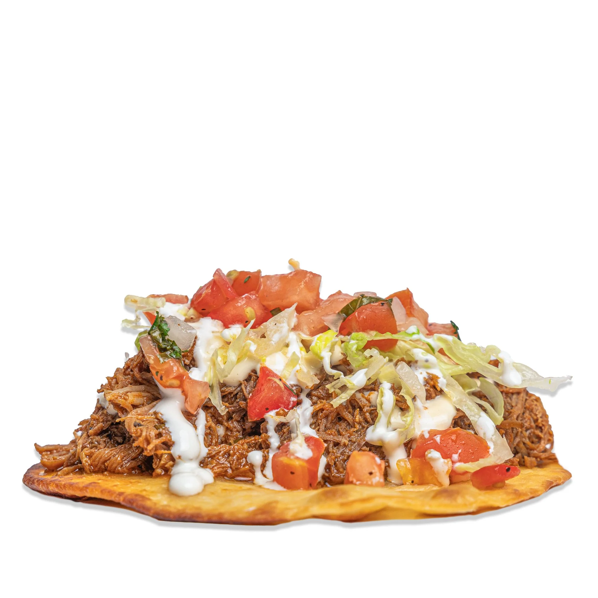 Tostada loaded with shredded beef, chopped tomatoes, shredded lettuce, and drizzled with white sauce.