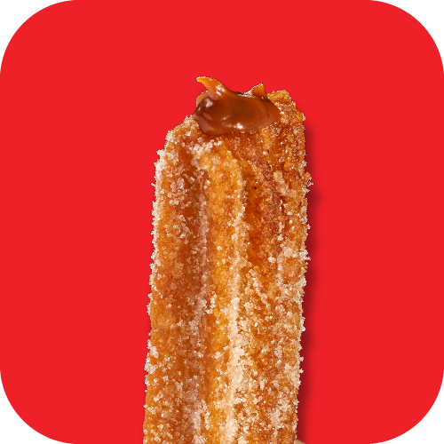 Close-up of a fried churro with cinnamon sugar, topped with caramel sauce, against a red background.