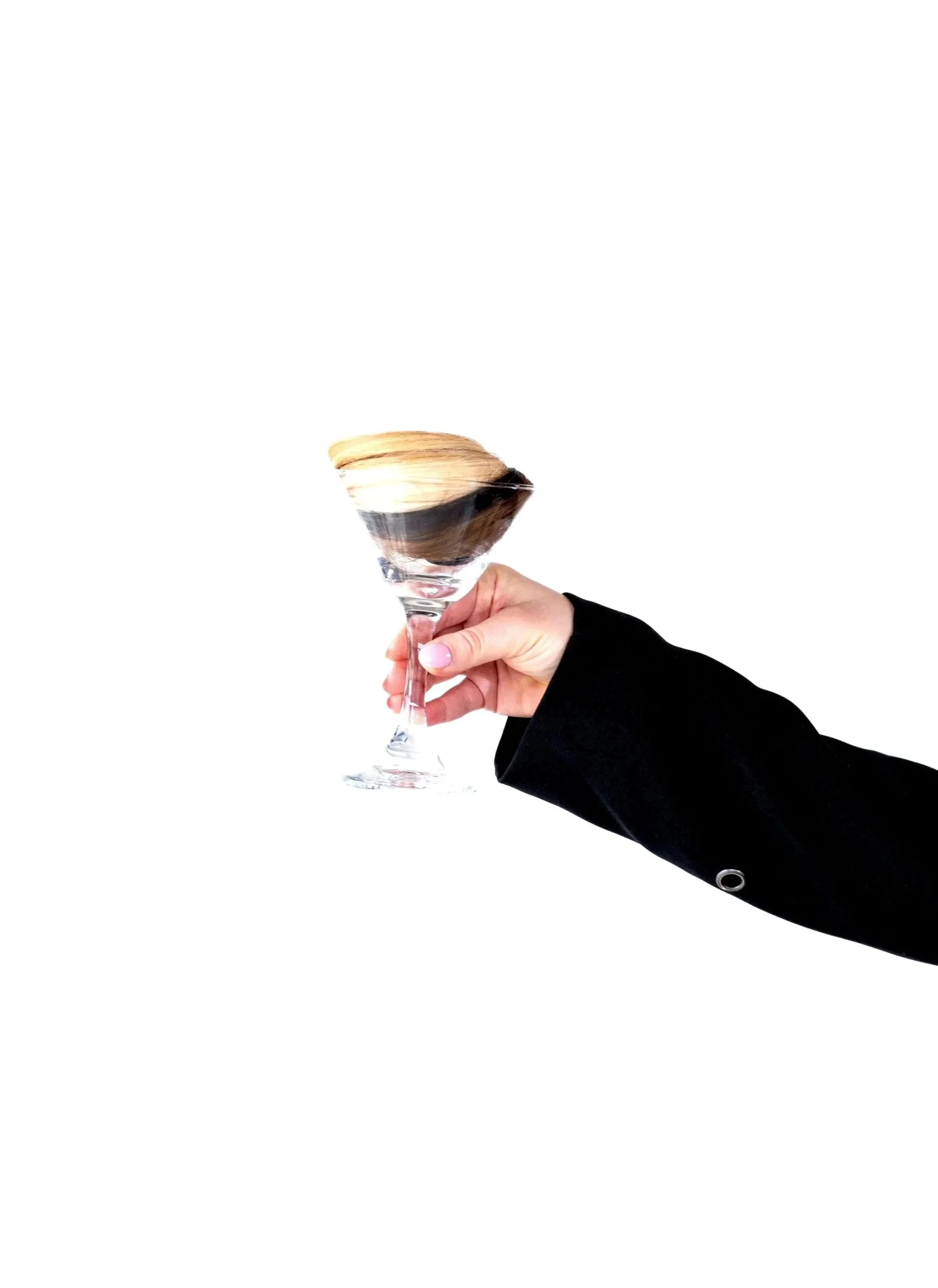 A hand with manicured nails holding a champagne glass filled with champagne, against a plain white background.