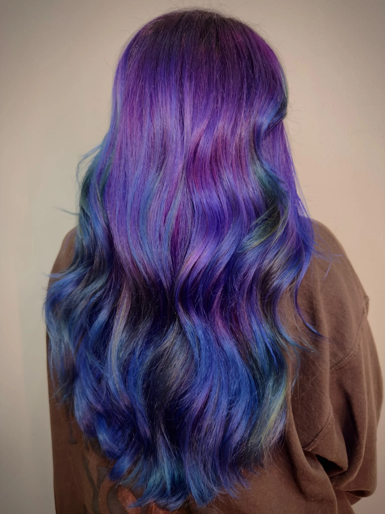 Back of a person with long, wavy hair dyed in purple, blue, and green shades.