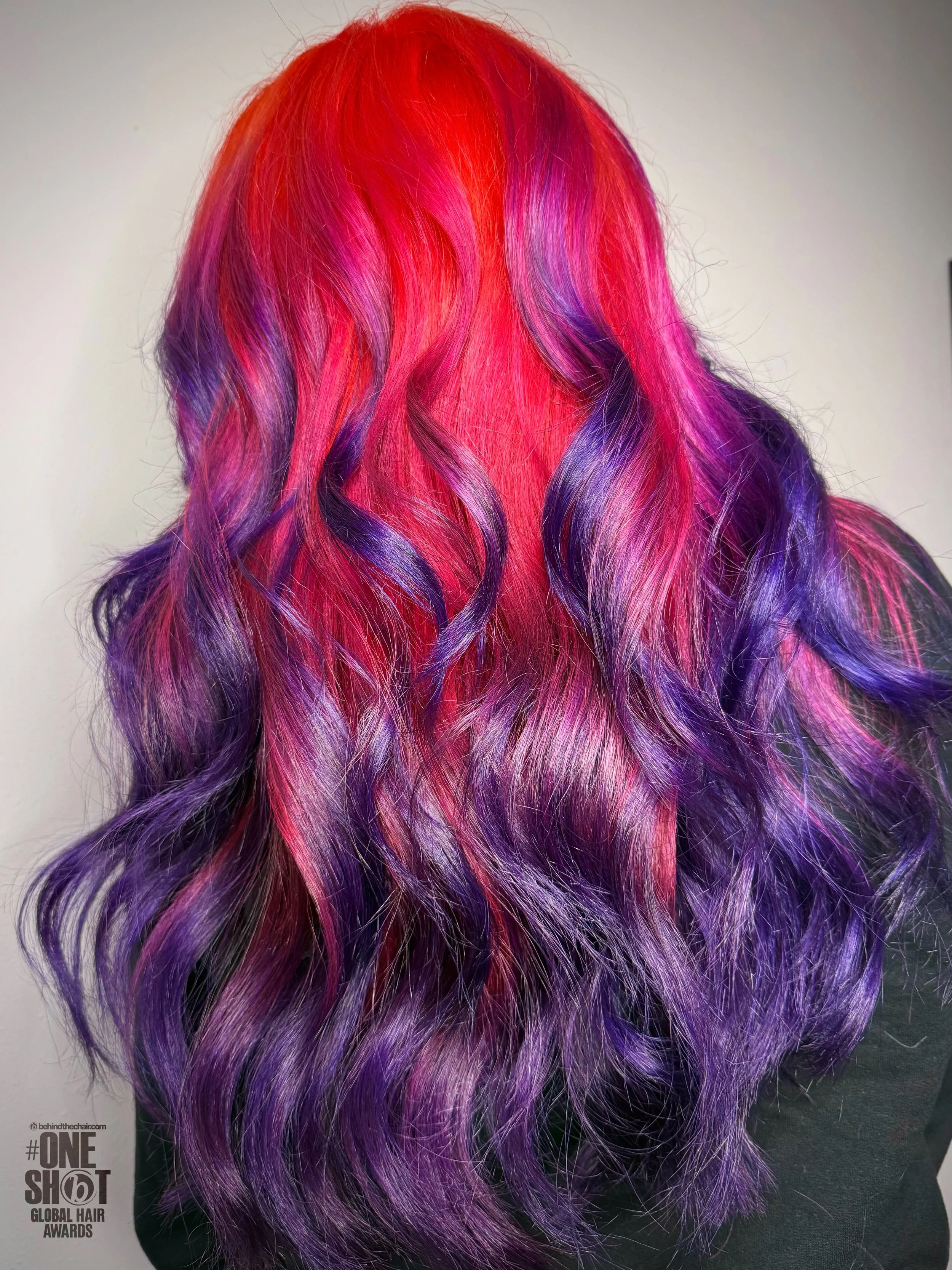 Colorful, long, wavy hair with shades of red, pink, purple, and violet, displayed against a neutral background.