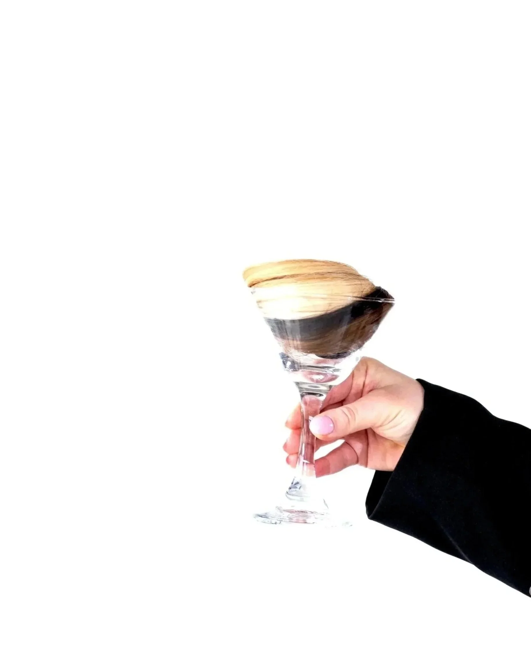 A hand holding a glass of champagne with a gold foil top and a black ribbon around the neck, against a white background.