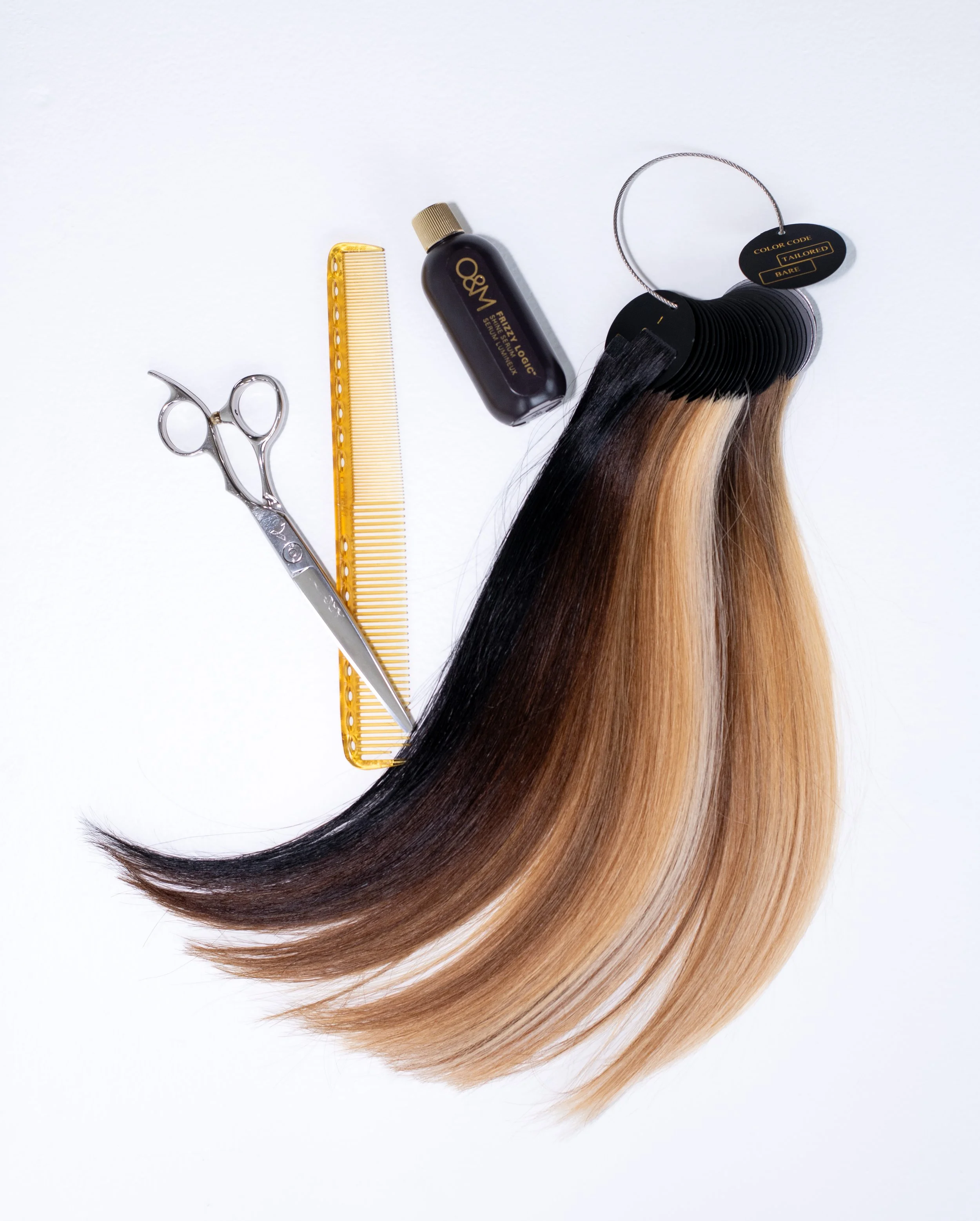 Cutting scissors, yellow hair comb, small bottle labeled 'WQ Frizz Logic', and hair extensions with black, brown, and blonde shades, arranged on a white surface.