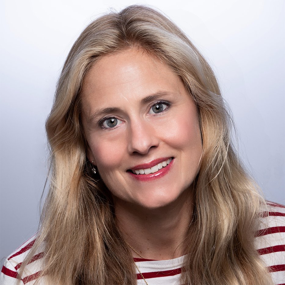 A woman with long blonde hair, blue eyes, and a bright smile, wearing a red and white striped top against a neutral background.