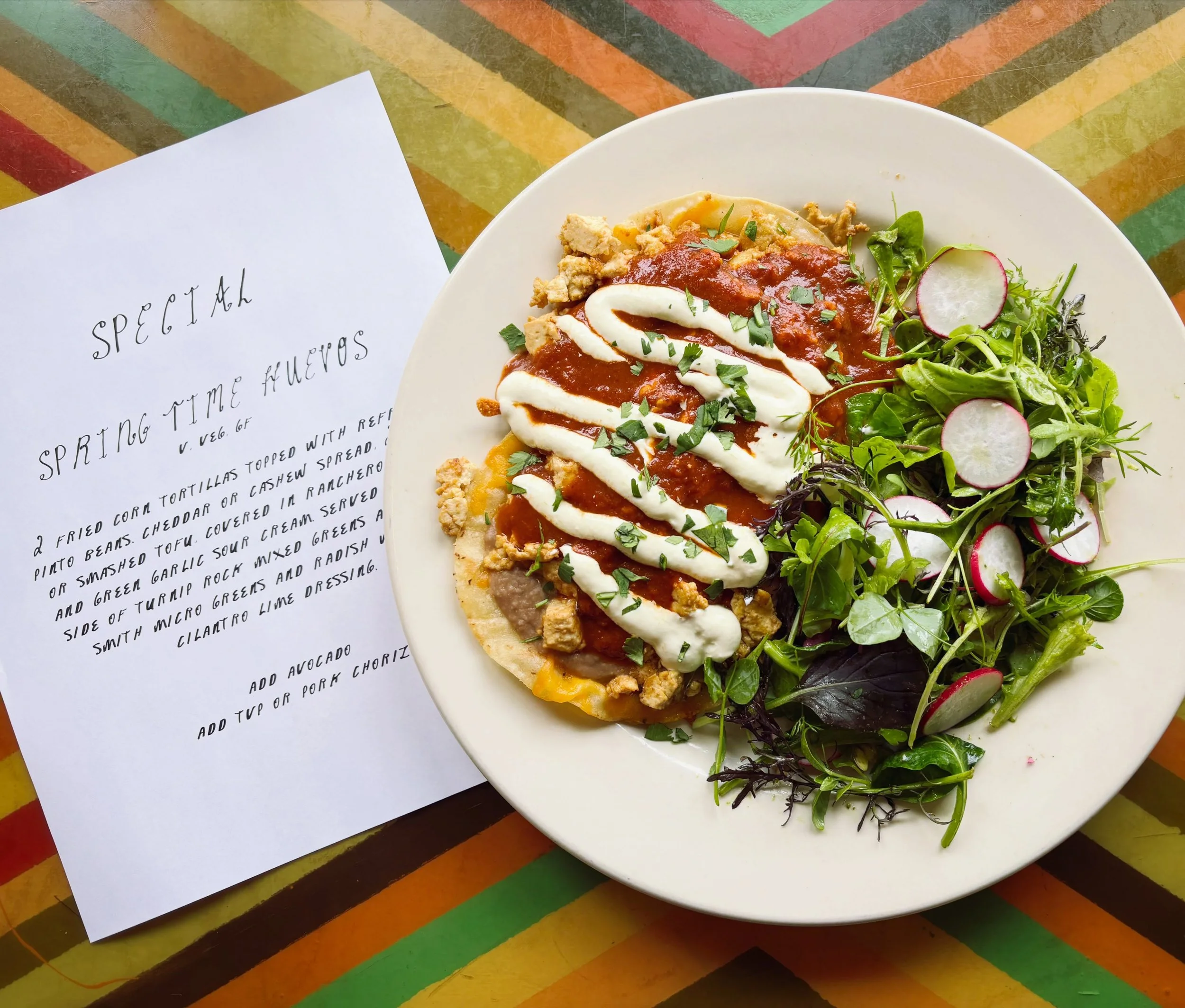 🌼SPRINGTIME HUEVOS🌼 2 fried tortillas topped with refried pinto beans, 2 eggs or tofu, cheddar or cashew spread, covered in ranchero sauce and green garlic sour cream. Served with a side of @turniprockcsa mixed greens and @dragsmith.farms microgree