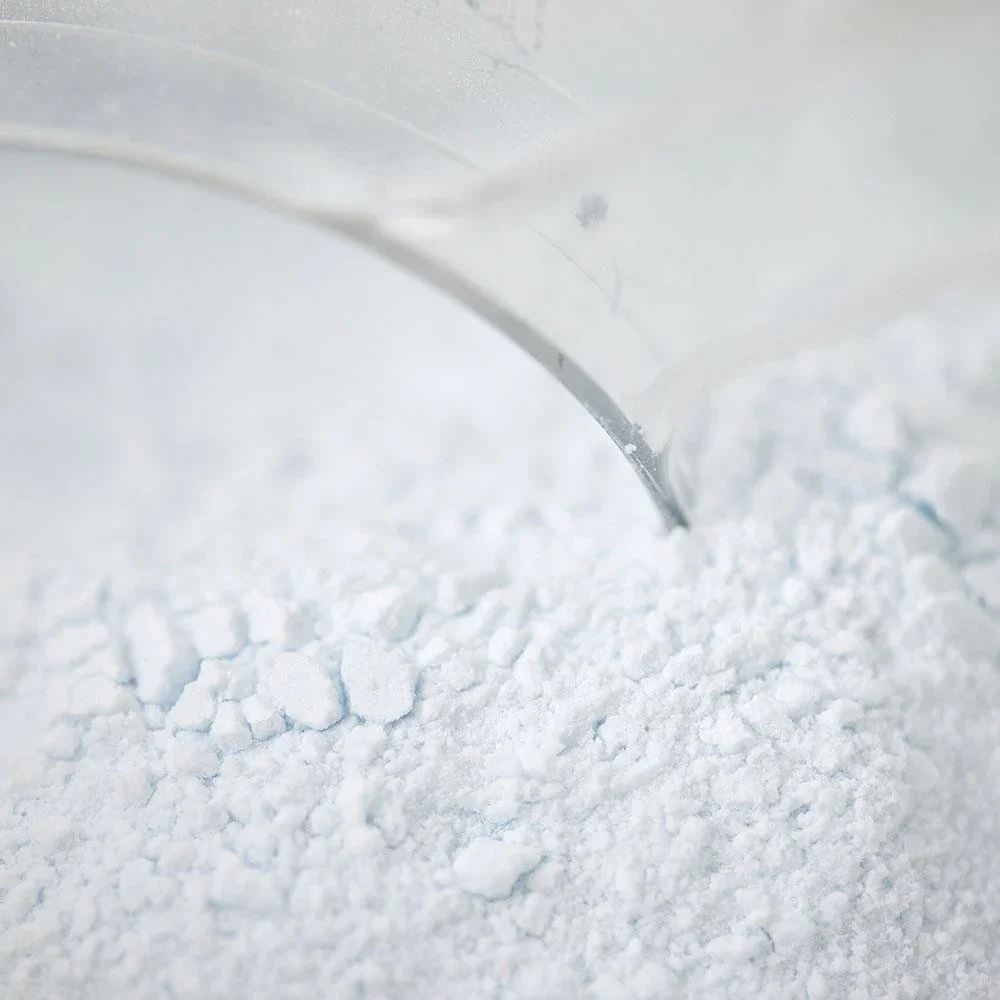 Polvo blanco finamente molido sobre una superficie, con un utensilio metálico en el borde de una taza del mismo color.