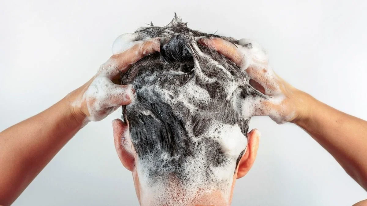 Persona lavando su cabello con champú, haciendo espuma en el cabello