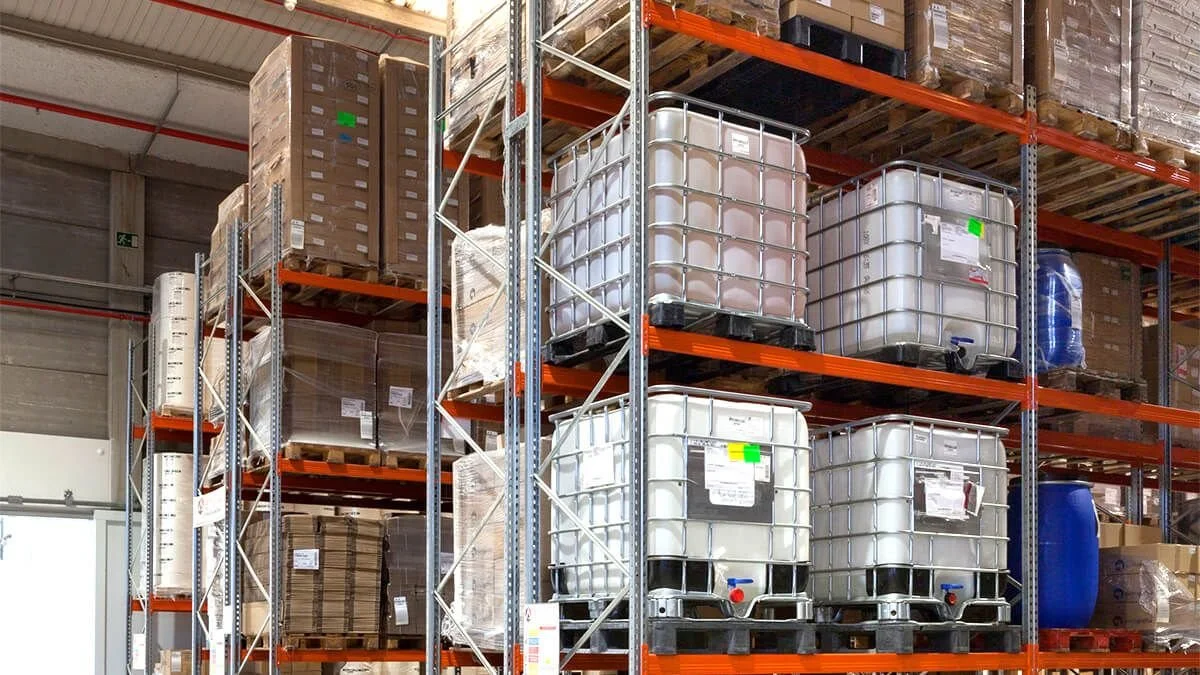 Estantería en un almacén con envases grandes de líquidos y cajas.
