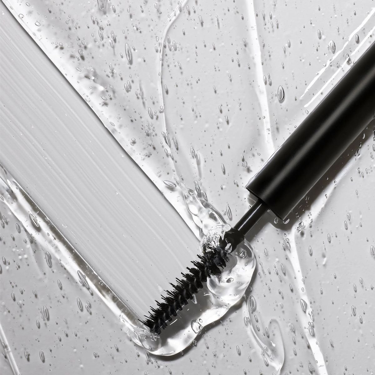 Rímel en una superficie metálica con gotas de agua, con el cepillo del rímel visible.