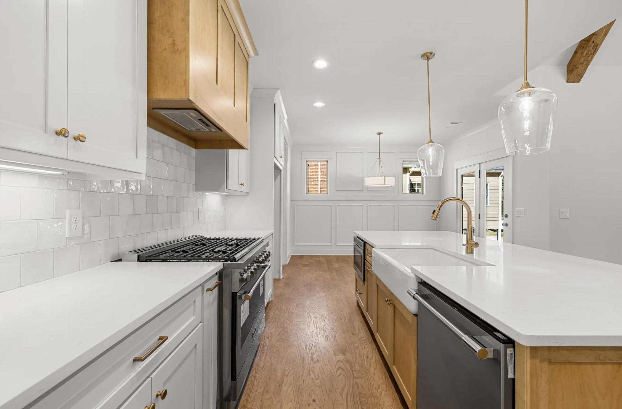 Modern kitchen with white cabinets, a gas stove, a white island with a farmhouse sink, pendant lighting, and hardwood flooring.