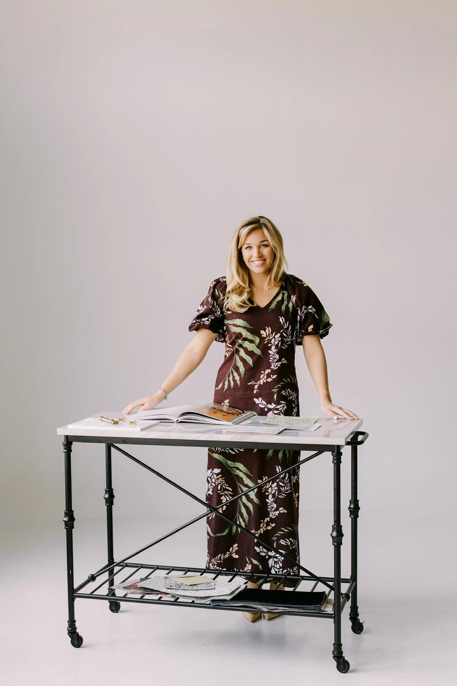 Woman standing behind a table with magazines and papers, smiling at the camera.