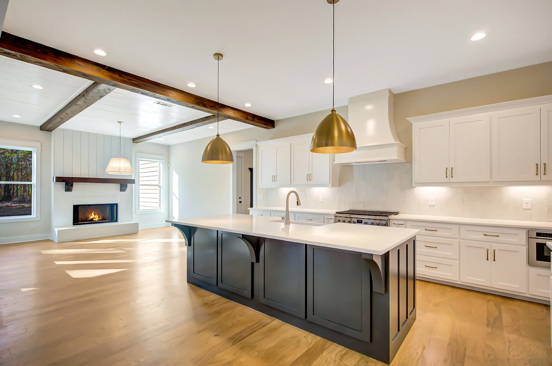 Modern kitchen with white cabinets, a large island with a dark base, gold pendant lights, a gas stove, and a fireplace in the living area.