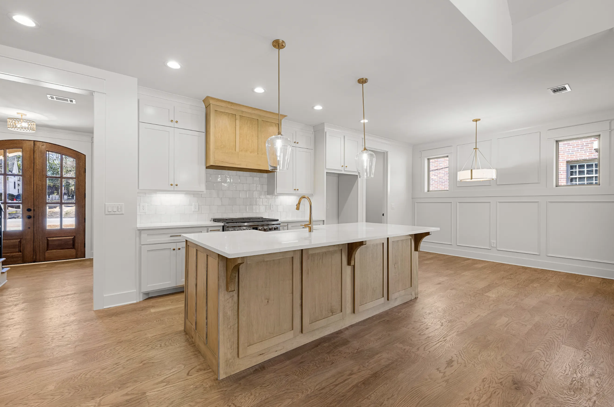 Empty modern kitchen with white and wood cabinets, a kitchen island with a white countertop, pendant lights, hardwood floors, all-white walls, and windows.