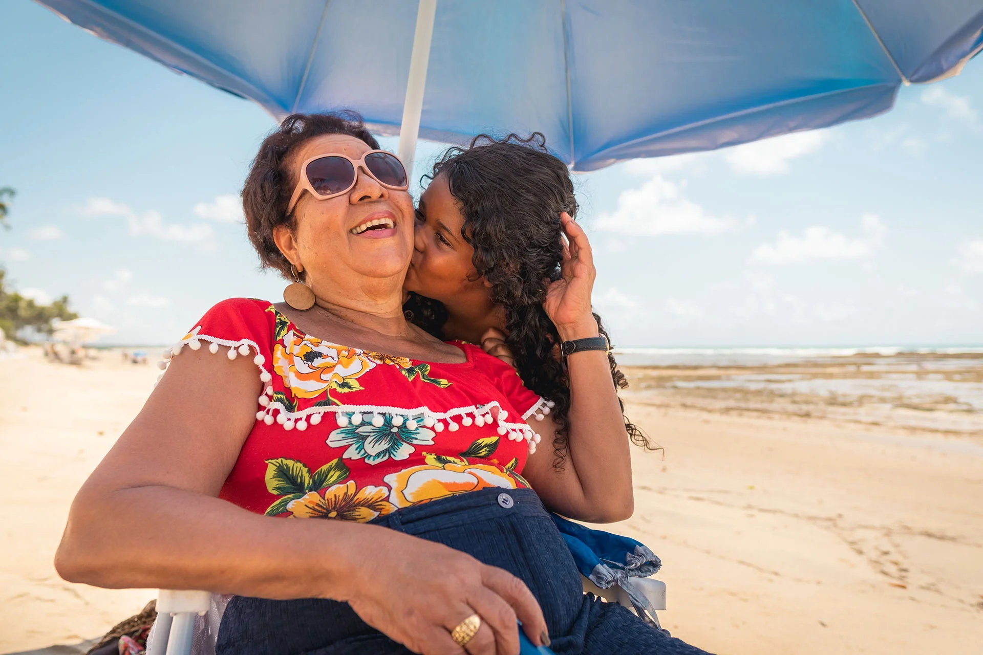 A woman and girl sitting under an umbrella on a beach.