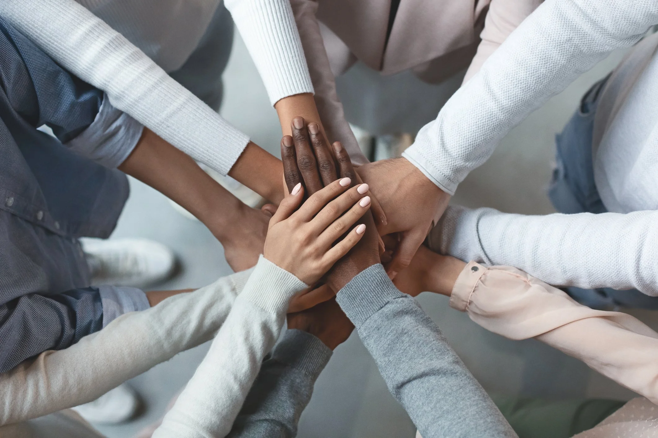 Multiple hands of diverse people stacked on top of each other in a gesture of unity or teamwork.