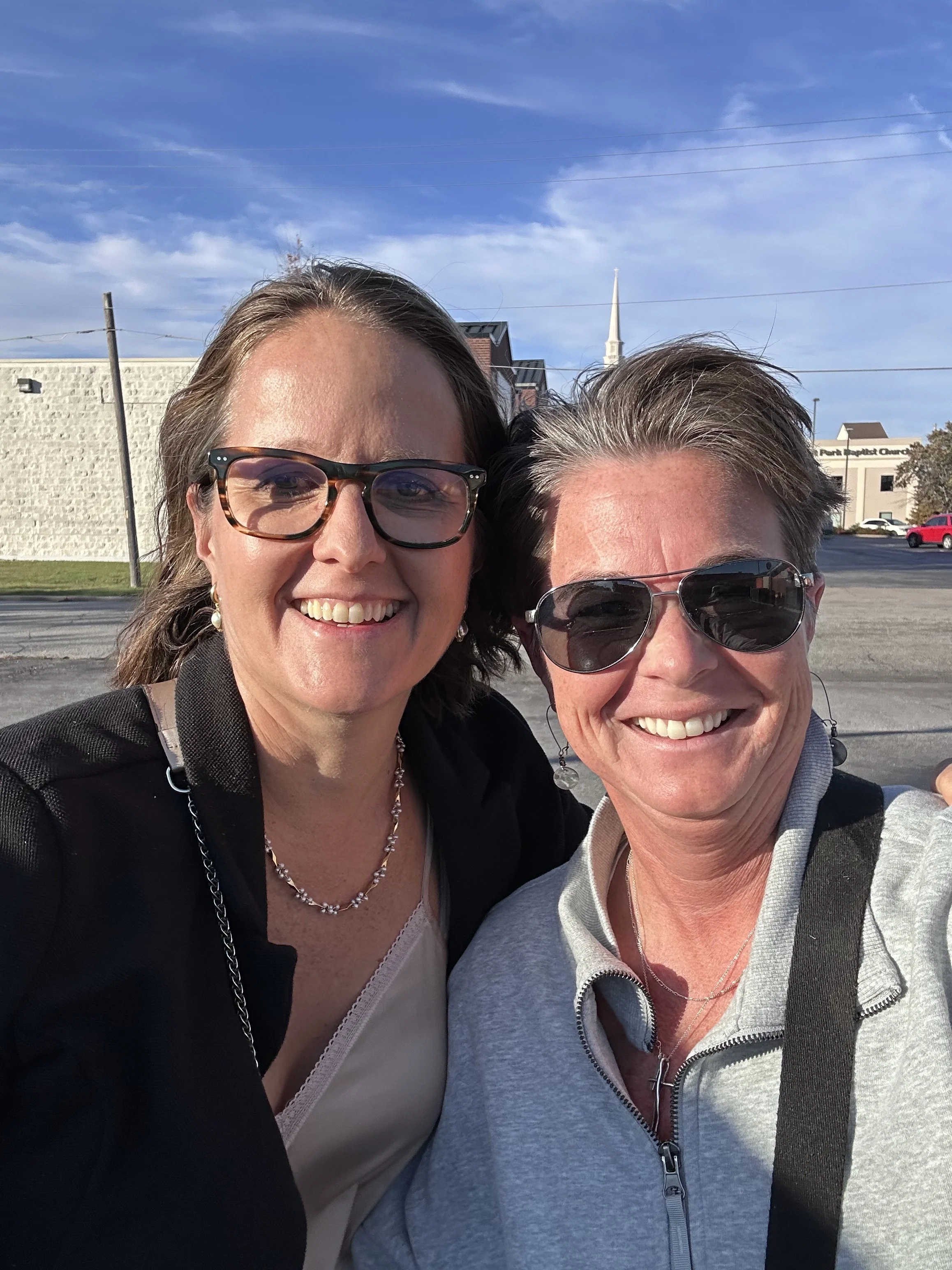 Lori and Gail Billman taking a selfie outdoors on a sunny day, with a blue sky and some clouds in the background..last time Lori picked up Gail from the airport coming home from treatment. 