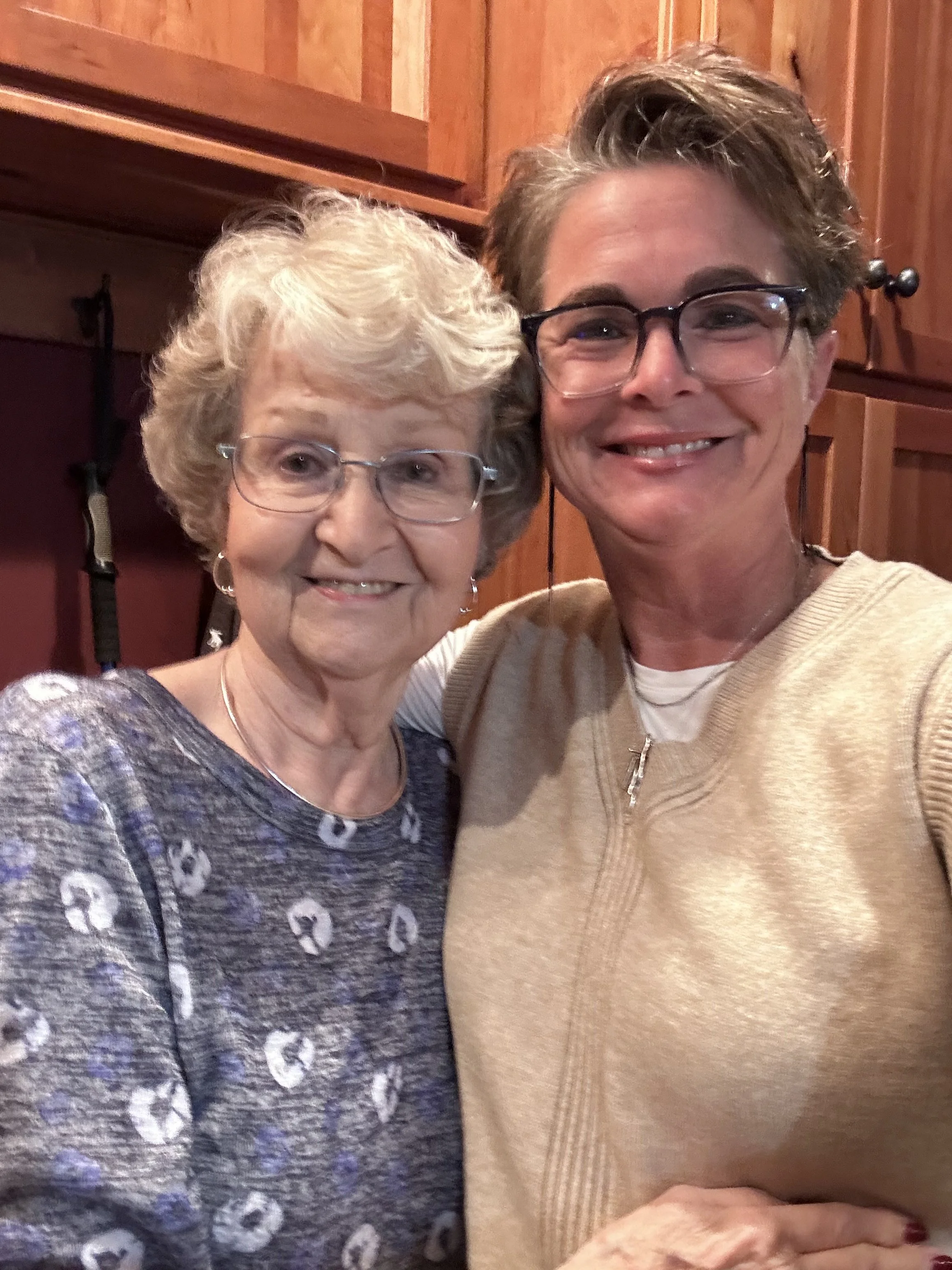Gail Billman and her mother, Betty smiling together for a selfie indoors with wooden paneling in the background.