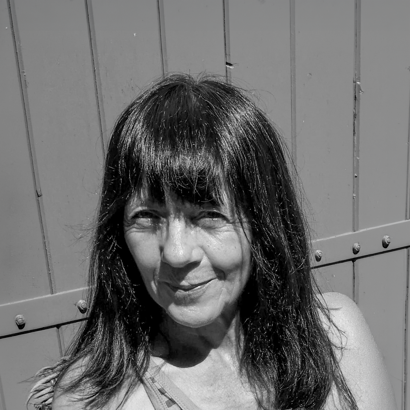Portrait en noir et blanc d'une femme souriante avec des cheveux longs et mi-longs, portant un maillot de bain, devant un mur en bois.