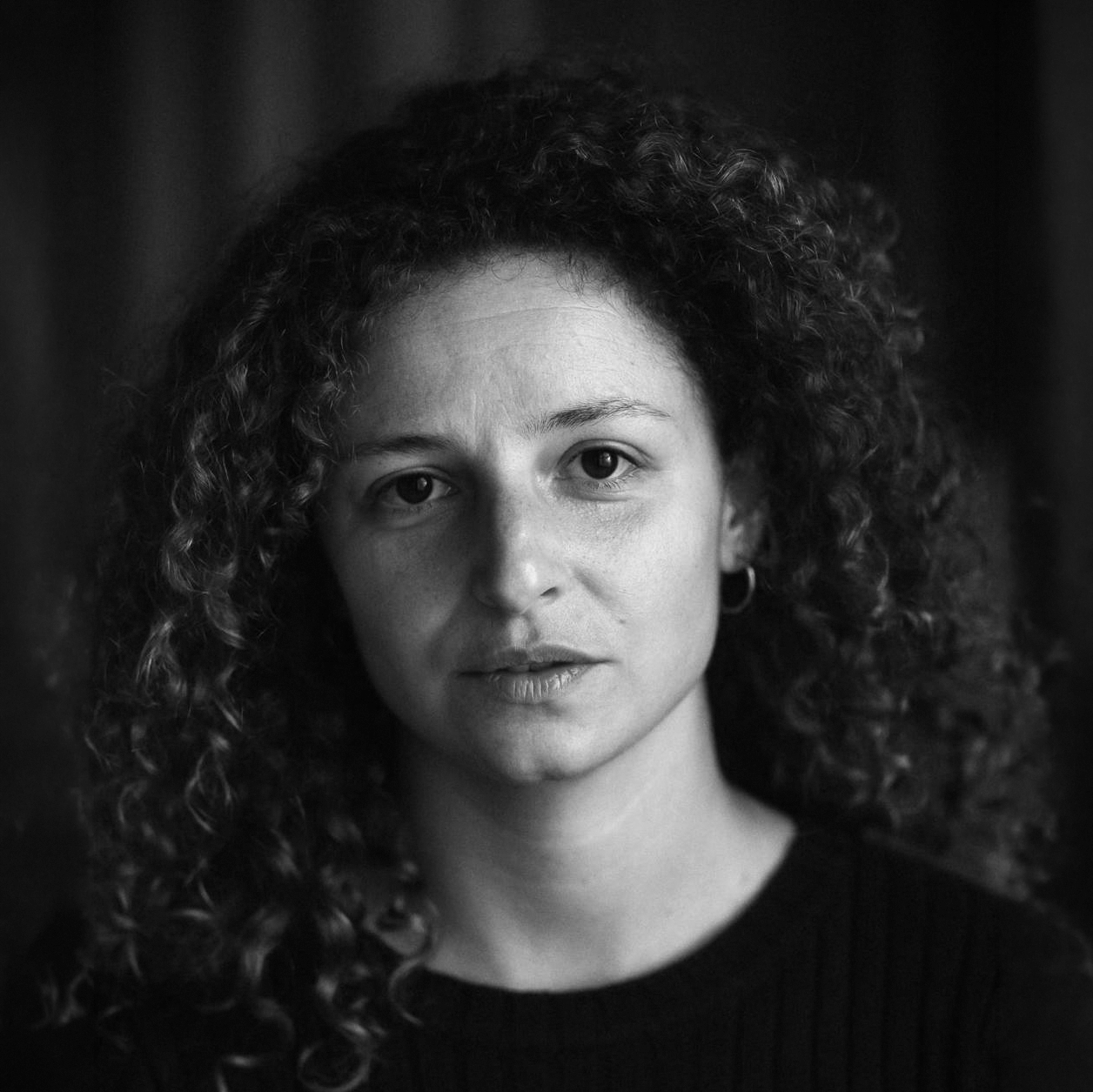 Portrait en noir et blanc d'une femme avec des cheveux bouclés, portant une veste noire et une boucle d'oreille.