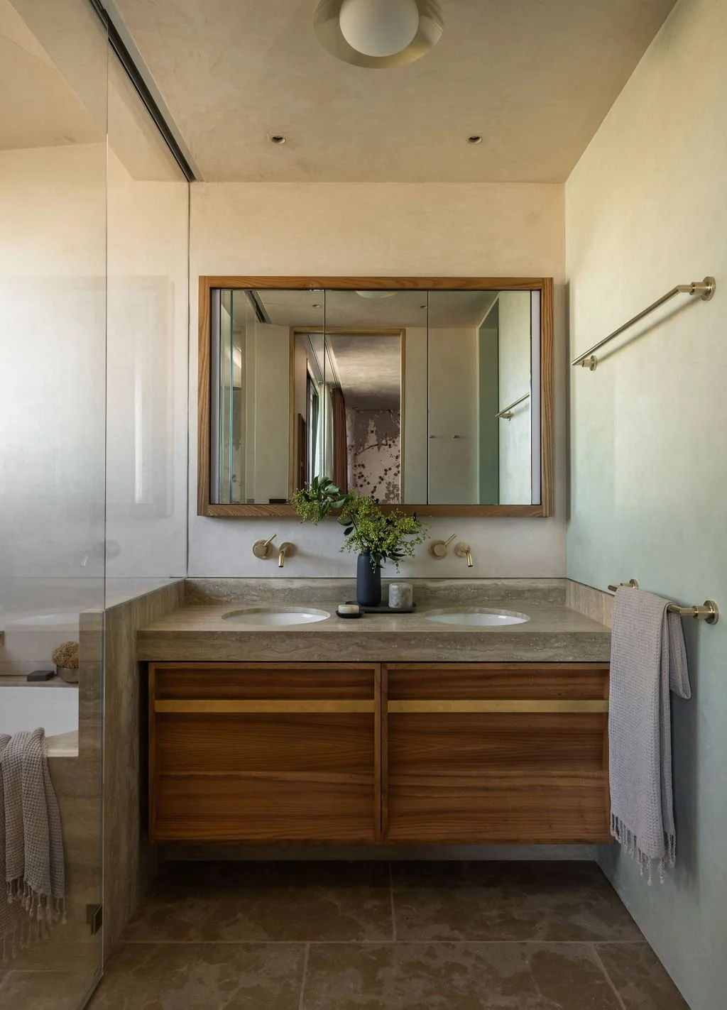 Modern bathroom with a double vanity, large mirror, vase with flowers, and beige tiles.
