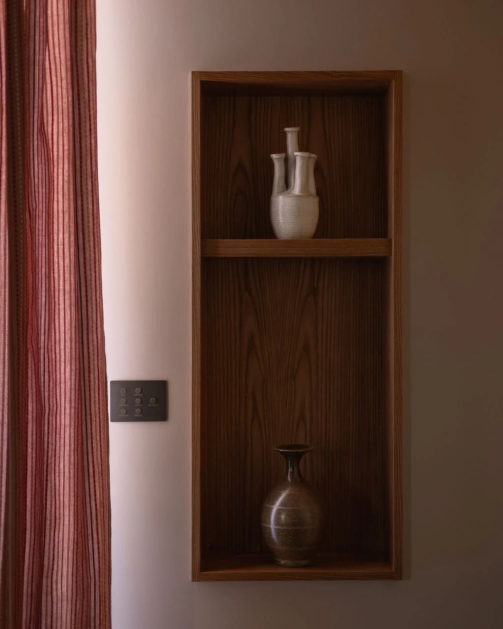 A wooden wall shelf with two ceramic vases, one on each shelf.