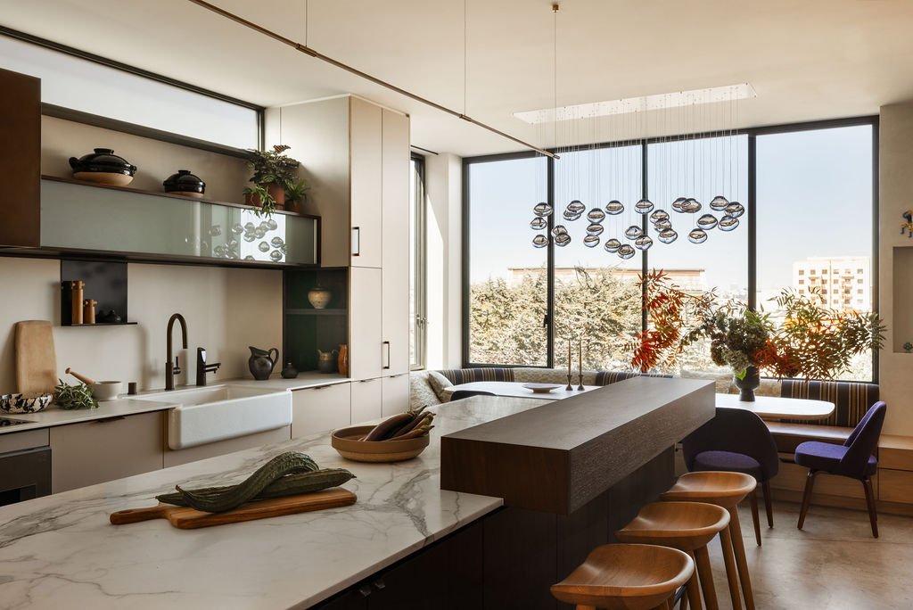 Modern kitchen and dining area with large windows, marble countertops, and a variety of plants and decorative items.