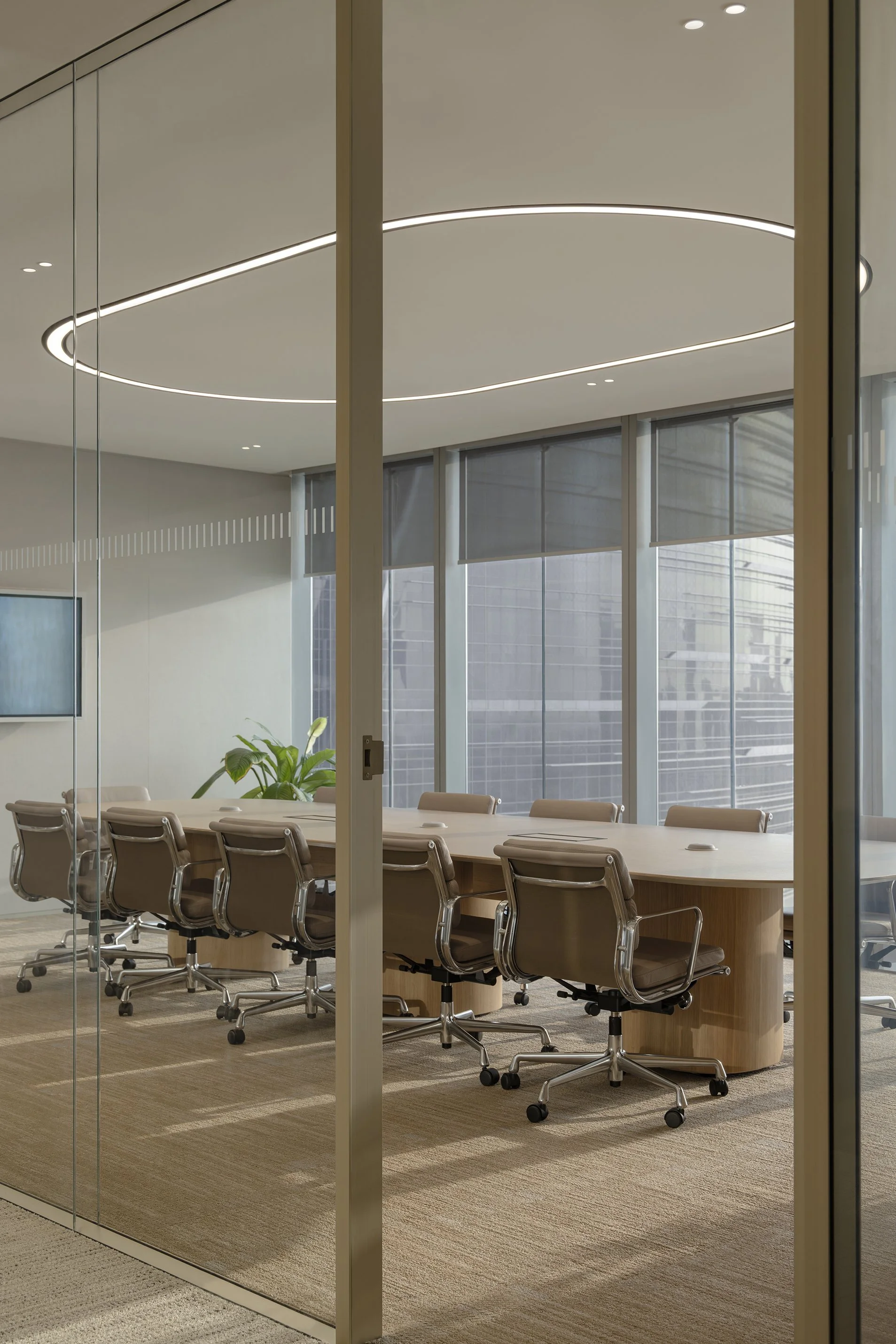 Modern conference room with a long wooden table surrounded by leather chairs, large windows with blinds, and a contemporary circular light fixture on the ceiling.