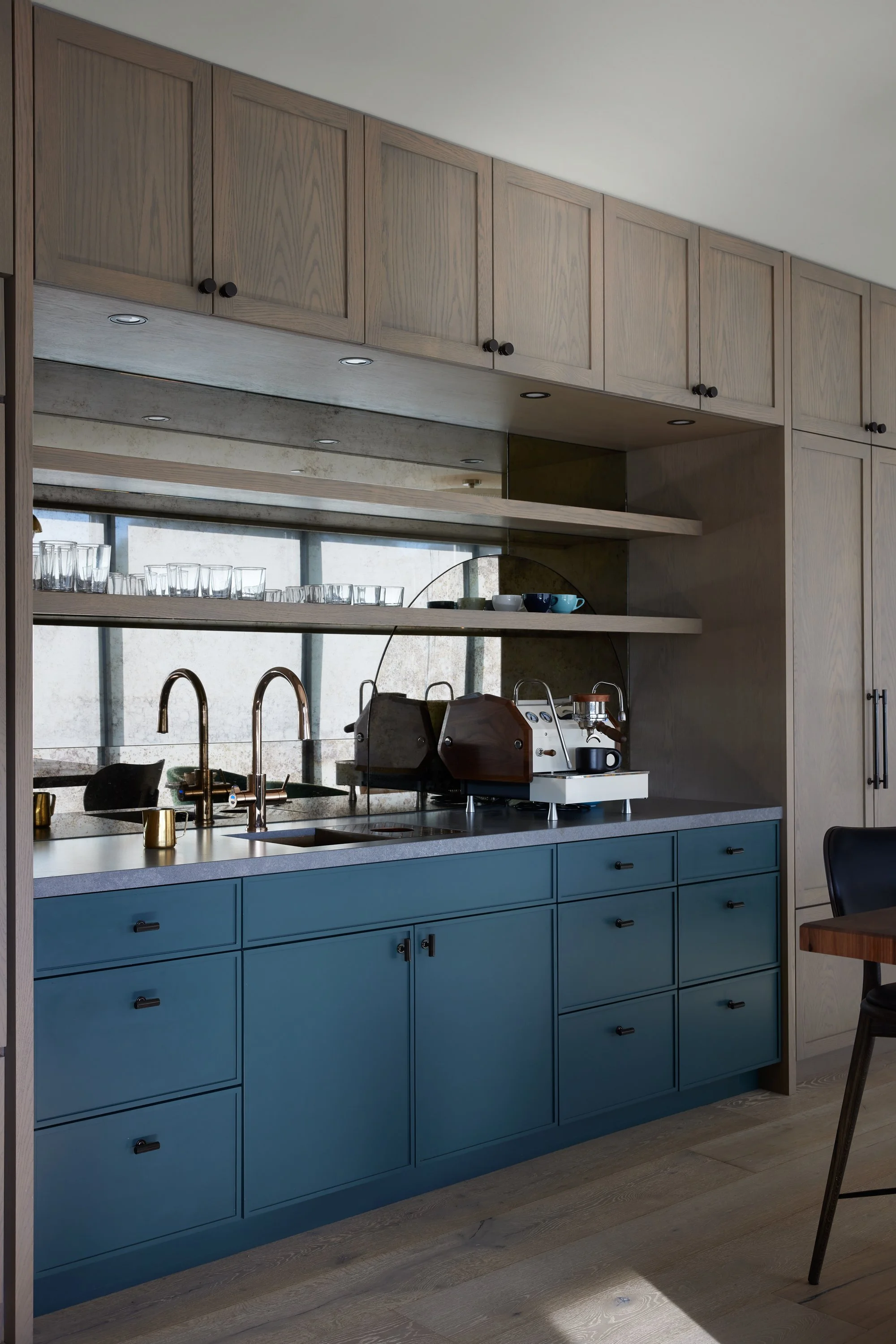 Modern kitchen with blue lower cabinets, wooden upper cabinets, a granite countertop, a sink with two faucets, and a coffee machine on the counter.