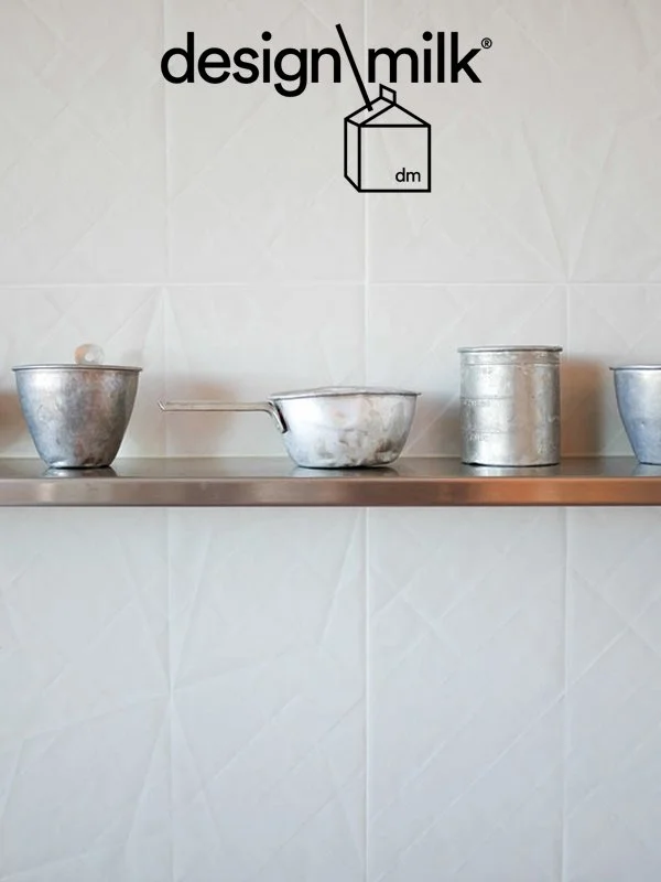 Metal kitchenware placed on a stainless steel shelf in front of a white tiled wall with the 'design milk' logo and an illustration of a milk carton above.