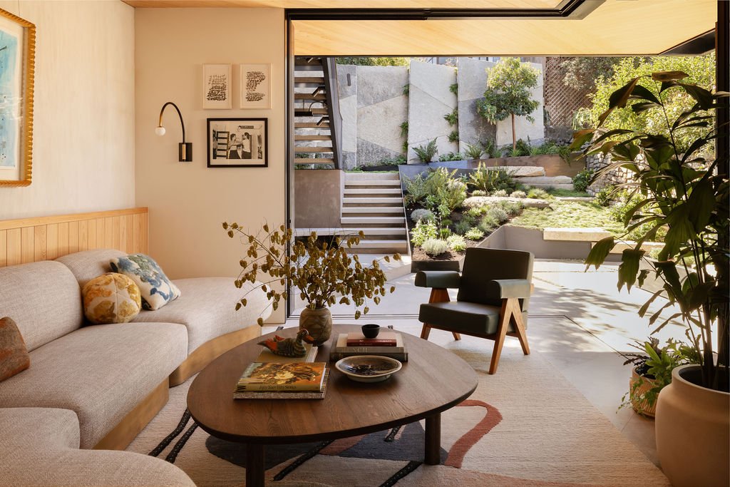Living room with large sliding glass door opening to a landscaped garden with stairs, trees, and plants.