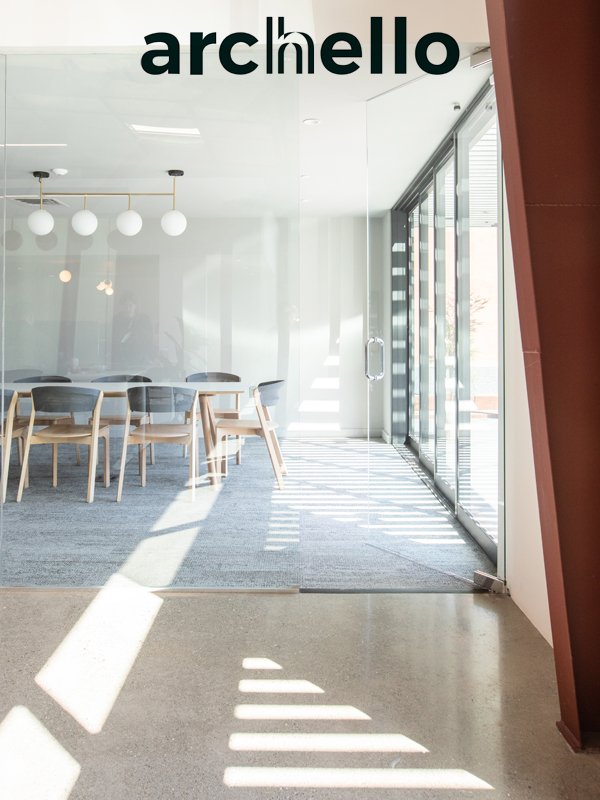 Interior view of a modern meeting room with a long table and chairs, illuminated by natural light through glass sliding doors, with artistic lighting fixtures on the ceiling and minimal decor.