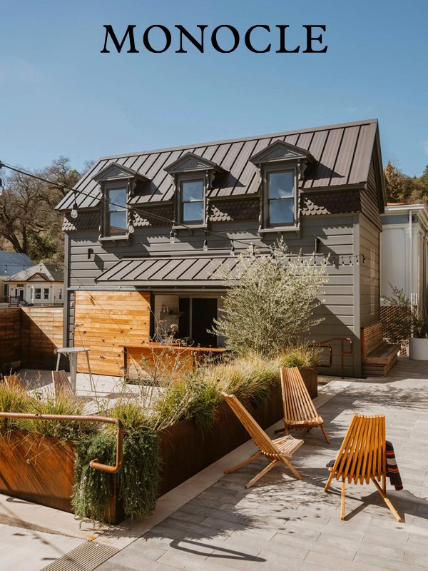 Modern gray house with three dormer windows, metal roof, and a small outdoor patio area with wooden chairs and planters.