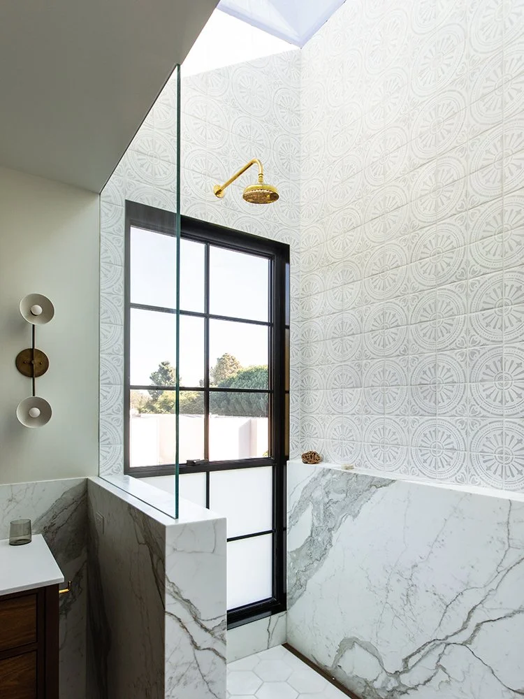 Bathroom with large window, marble wall and half wall, gold shower head, skylight, and modern wall decor.