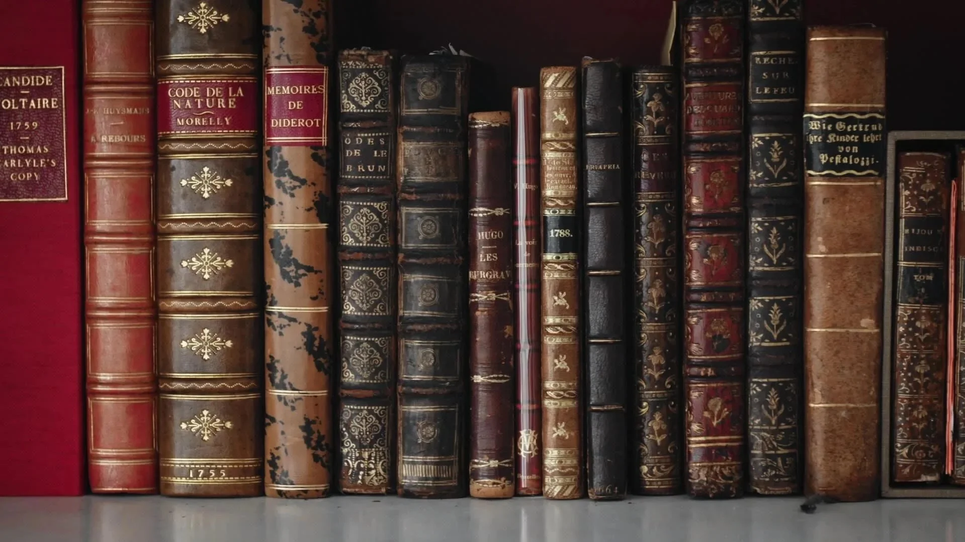 A row of old, leather-bound books with ornate gold and black designs on the spines, arranged on a shelf.