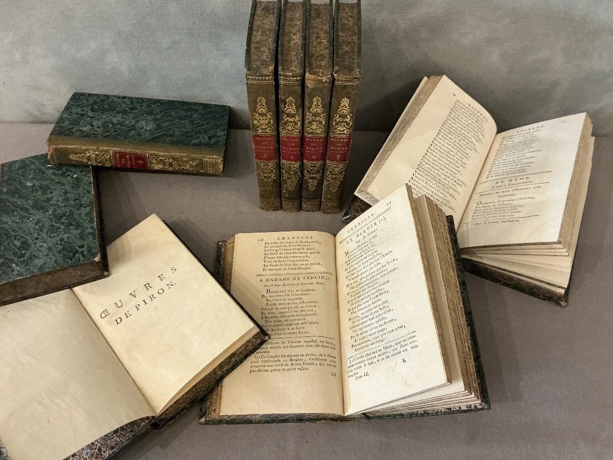Several antique books, some open and some closed, with green marble-patterned covers and ornate binding, displayed on a light gray surface.